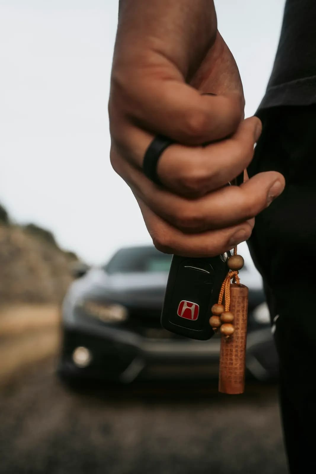 Hand holding car keys with a car in the background