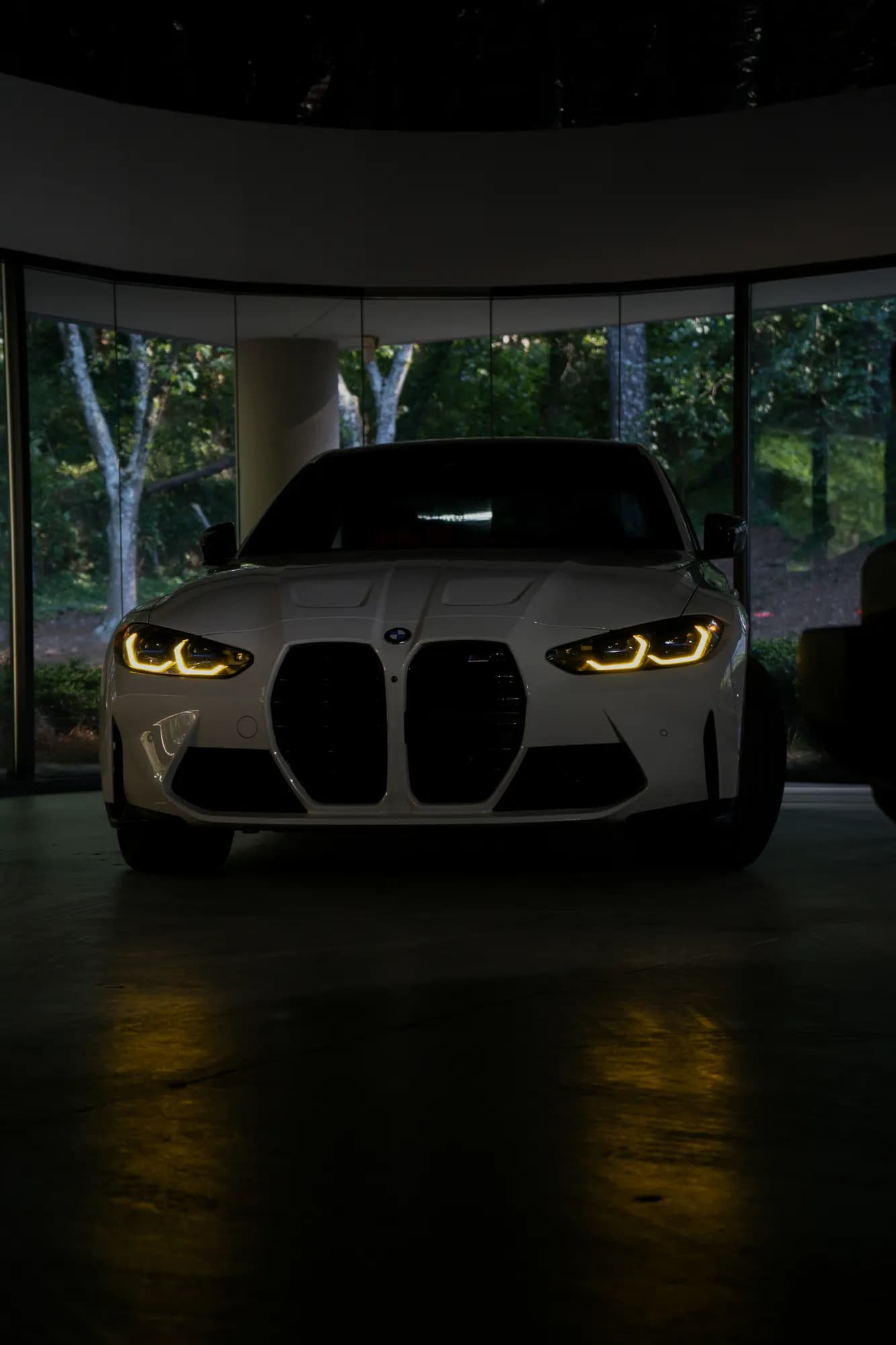 White BMW M4 with headlights on in a dark showroom