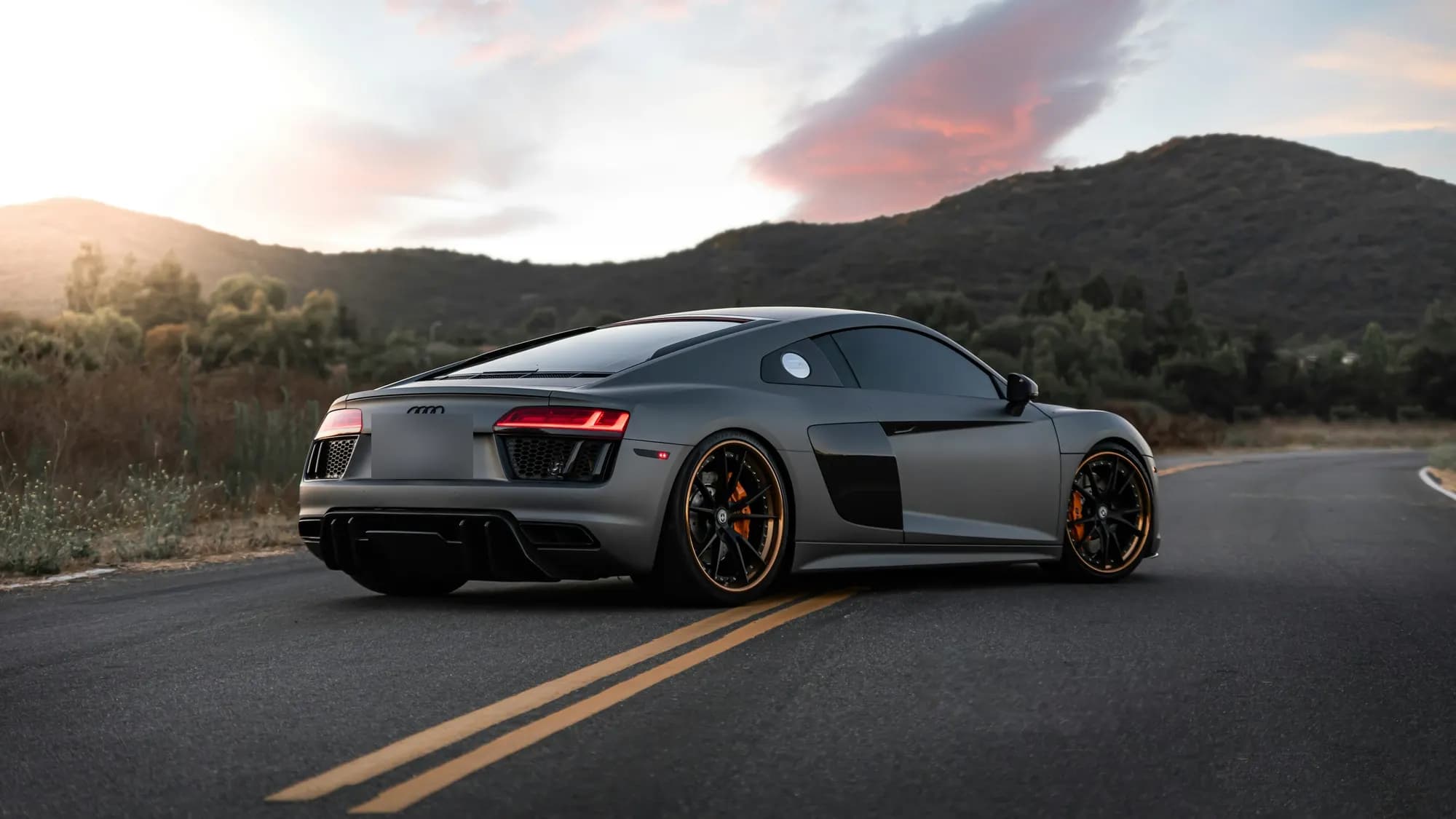 Matte grey Audi R8 on a winding road at golden hour, rear three-quarter view