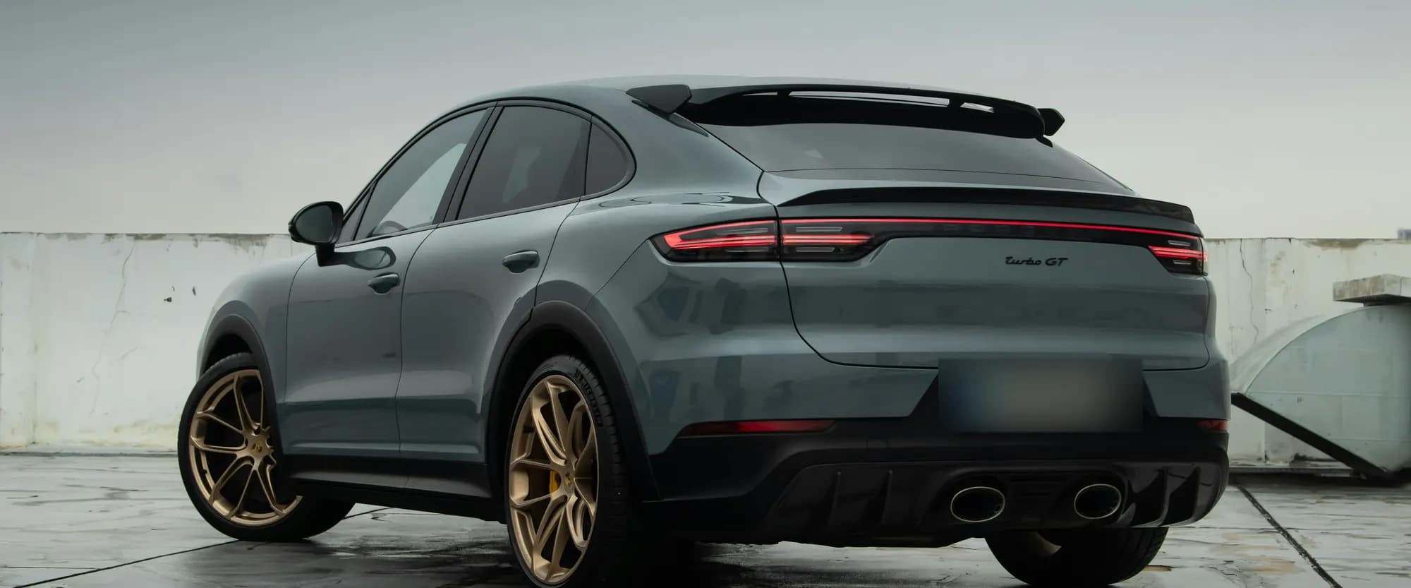 Grey Porsche Cayenne Turbo GT, rear three-quarter view on wet concrete