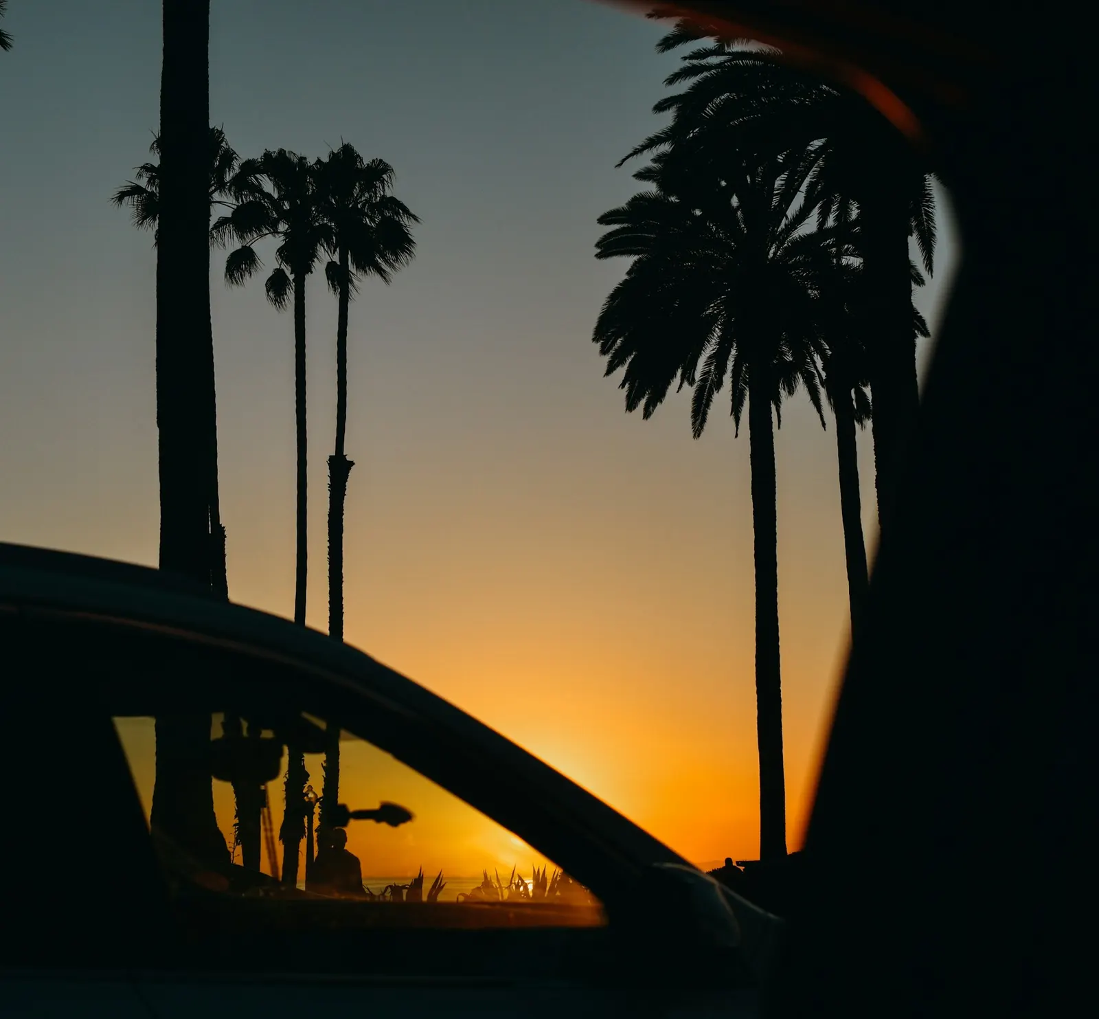 Car silhouette framed by palm trees at sunset